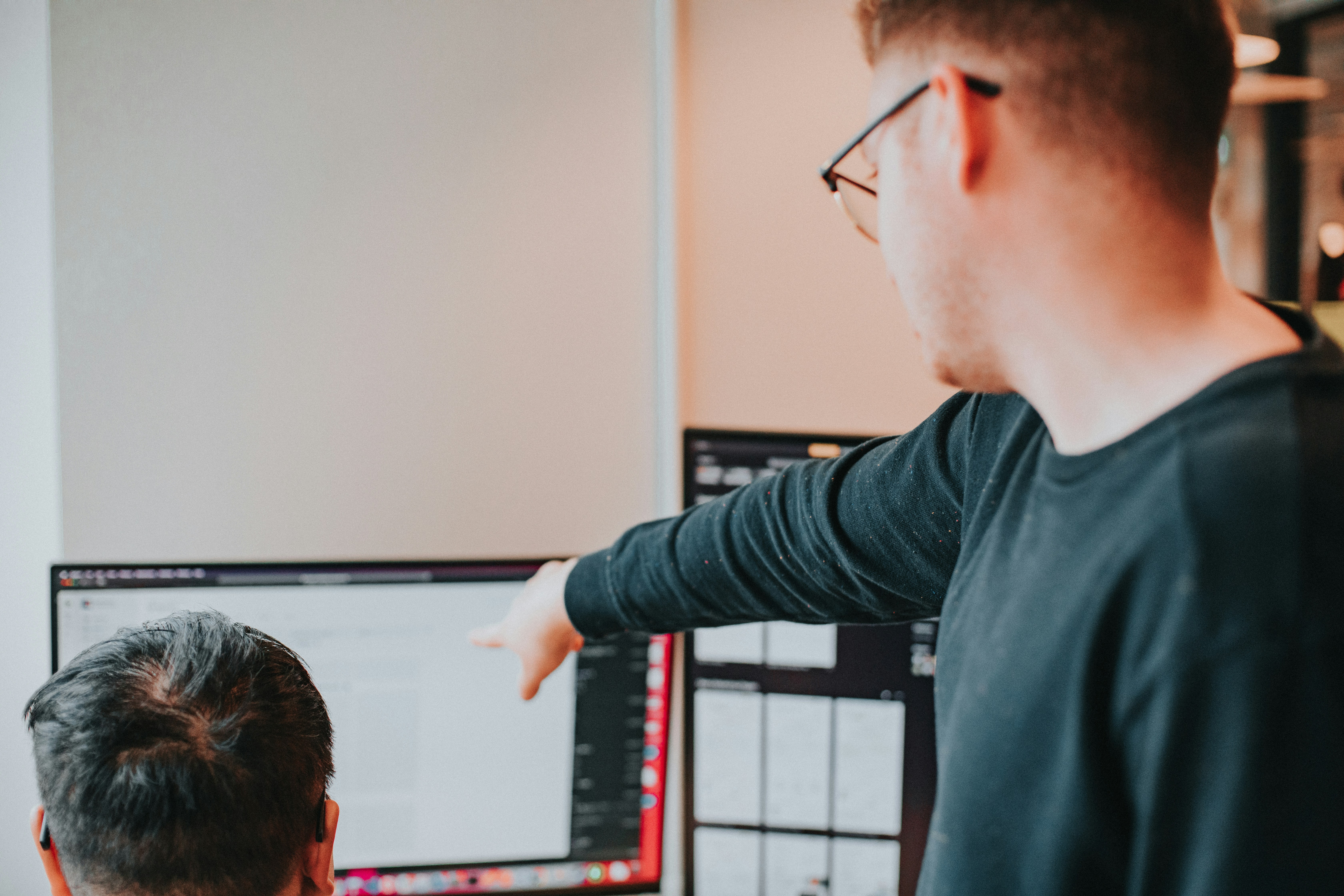 Two colleagues collaborating at a desk, one pointing at data on a computer screen while the other looks on.